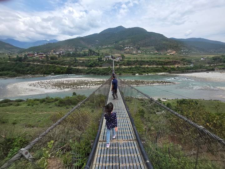 People walk across a long swaying suspension bridge high above a turquoise river and valley.