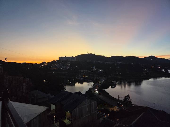 A tranquil lake and hillside town glow in the colors of dusk with car lights tracing the shoreline road.