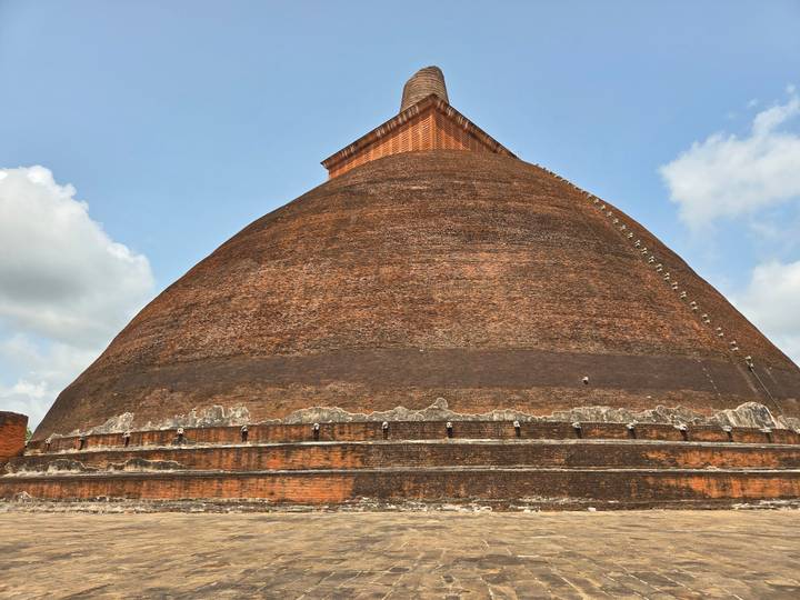 Massive brick stupa rises against a pale sky, showing weathered terracing and a narrow staircase to the pinnacle.