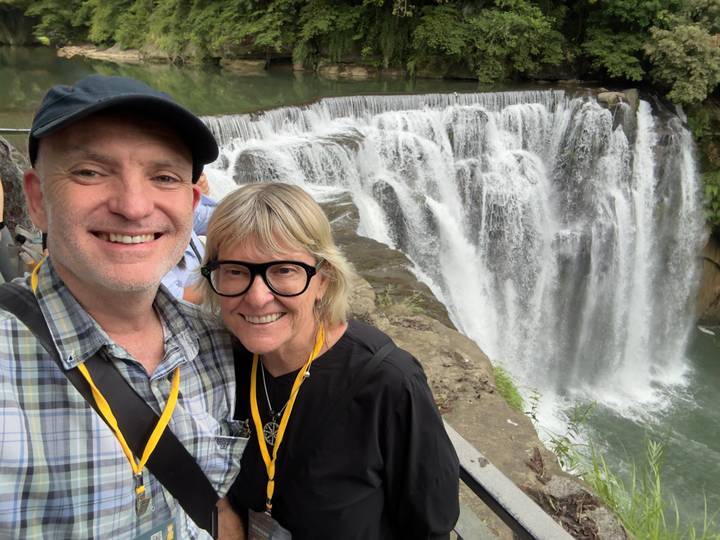 A smiling couple poses for a selfie in front of the cascading Shifen Waterfall in Taiwan.