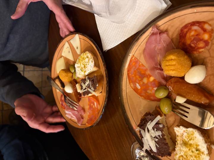 Two appetizer plates display assorted Sicilian meats, cheeses, olives and croquettes on a wooden table.
