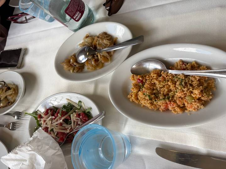 A selection of couscous, caramelized onions and salad dishes spread across a restaurant table.