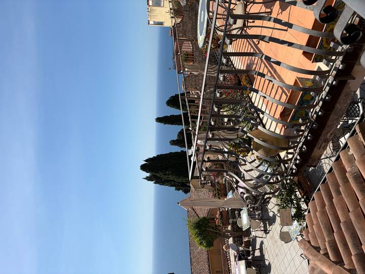 A Mediterranean terrace with wrought-iron railings overlooks the deep blue sea and distant cypress trees.