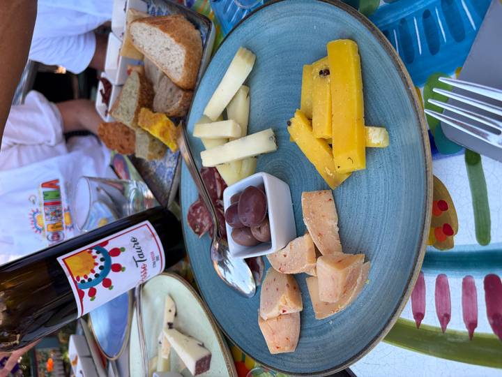 Rustic antipasto plate with cheeses, olives and bread on a colourful table while diners pour wine in the background