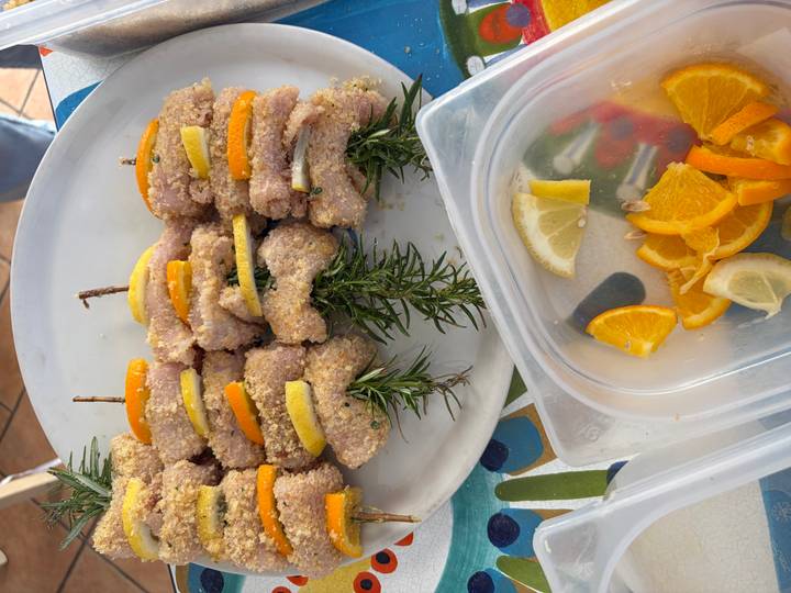 Raw meat skewers layered with orange and lemon slices and rosemary sprigs arranged on a white plate