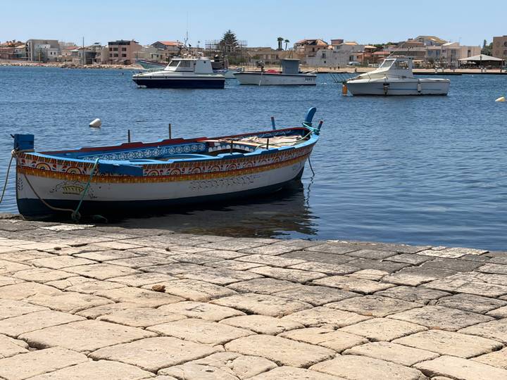 Traditional painted fishing boat floating on calm blue harbour water with other small boats and a coastal town behind
