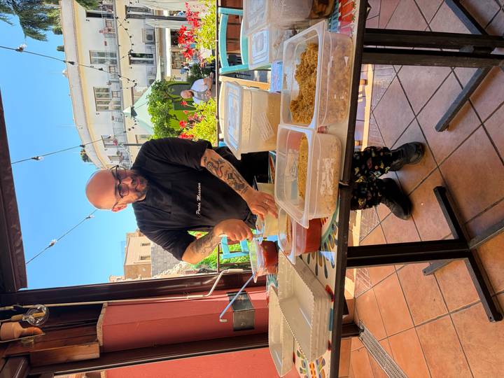 Chef mixes ingredients at an outdoor prep table surrounded by tubs of sauce and breadcrumbs