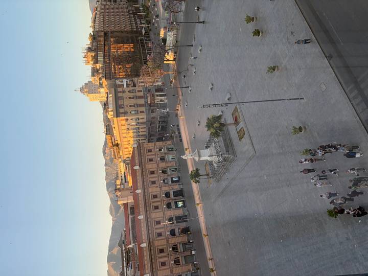 Elevated view of a grand city square with central statue and distant mountains in soft evening light
