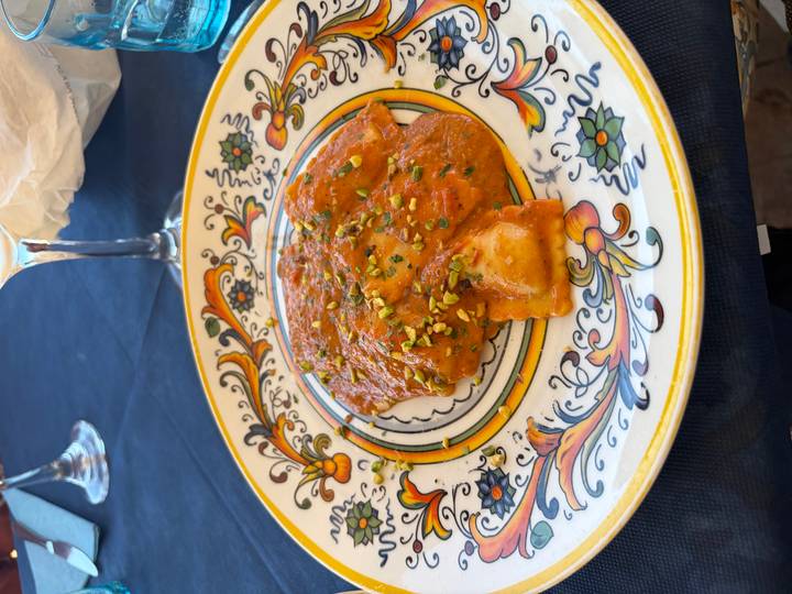 Decorative ceramic plate of ravioli topped with pistachio crumble in a creamy tomato sauce
