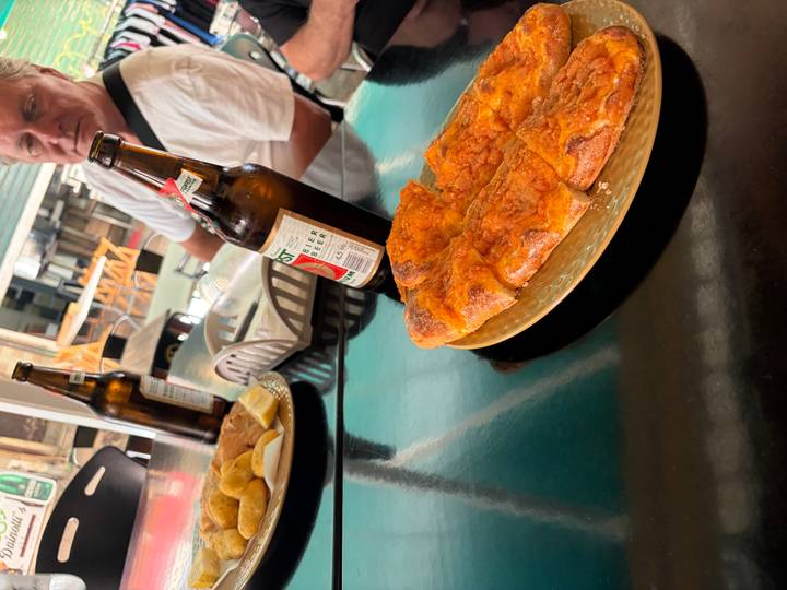 Rustic pizza slice and beer bottles on a dark café table with a diner in background