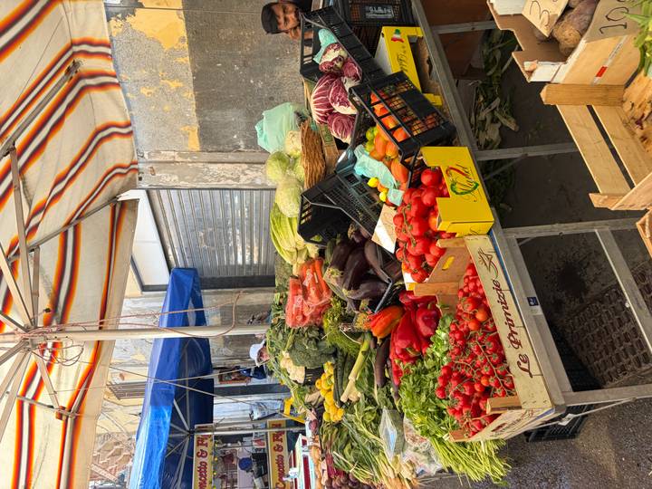 Outdoor produce stall piled high with tomatoes, peppers and leafy greens under a striped canopy