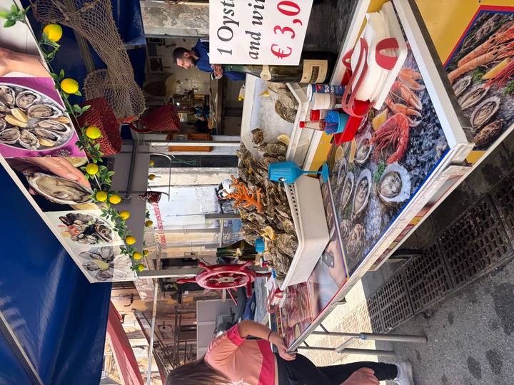 Seafood stand with fresh oysters on ice, bright lemon decorations and vendor in the background