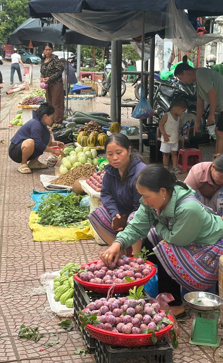 Local women sit among colorful piles of fruit and vegetables at an open-air market stall