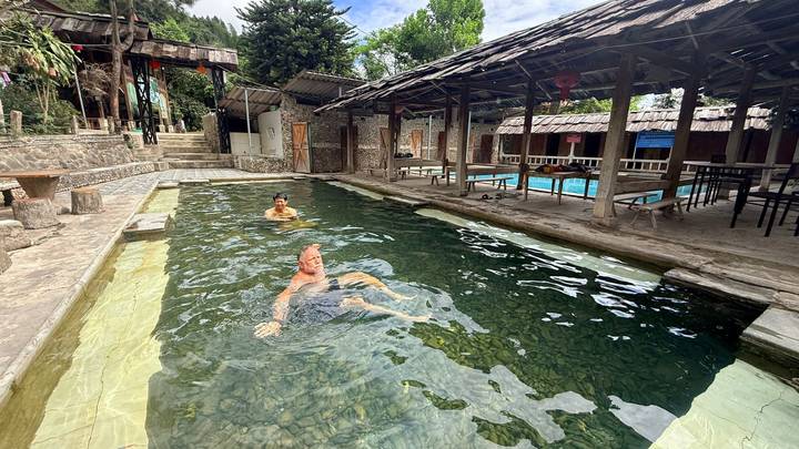 Two travelers relax and swim in a rustic outdoor stone pool with clear spring water