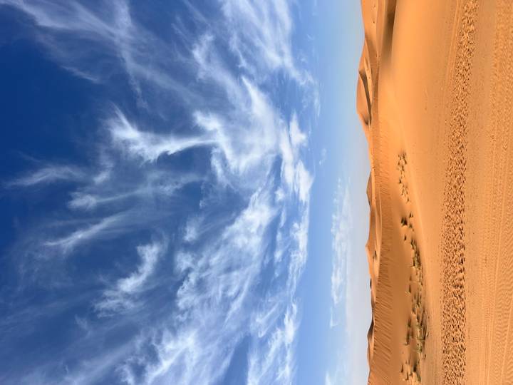 Vast desert landscape with bright orange dunes beneath a deep blue sky streaked with wispy clouds