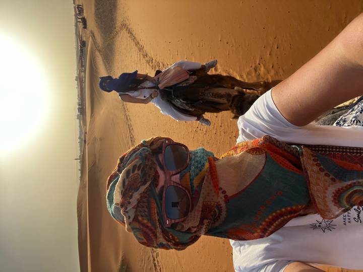 Selfie of two travelers on camels wearing colorful scarves and sunglasses crossing sun-lit desert
