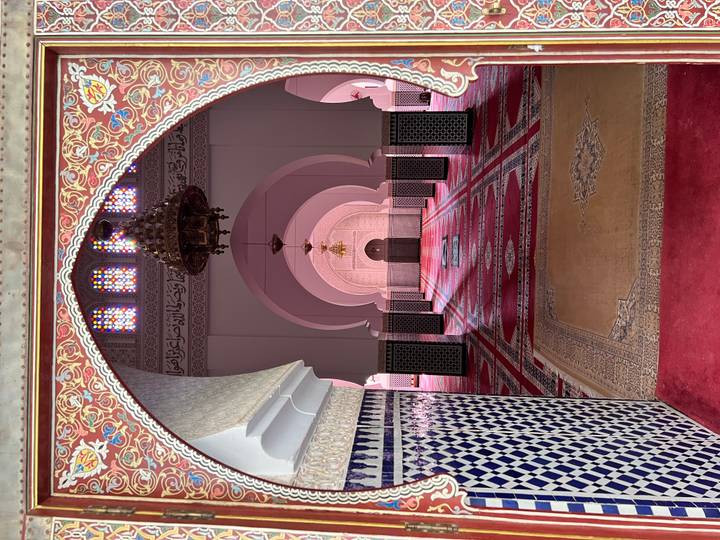 Opulent Moroccan mosque interior with ornate arches, patterned tiles, and deep red carpets