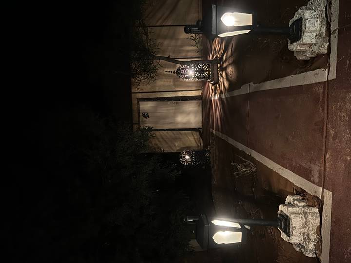 Dimly lit night pathway leading to a simple desert cabin entrance flanked by lanterns
