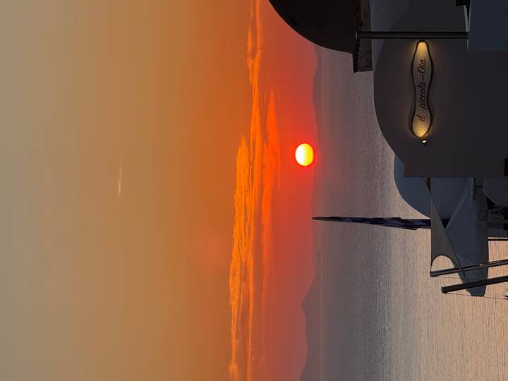Fiery orange sun sets into the Aegean Sea above Santorini’s cliff-top rooftops.