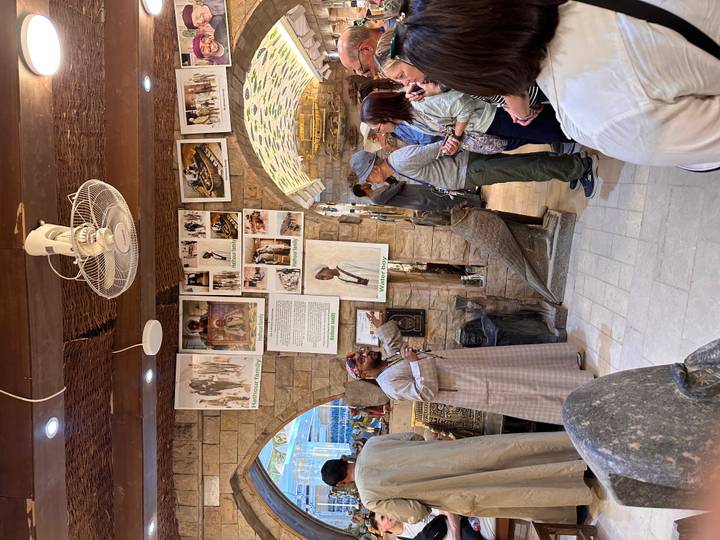 Local presenter explaining artifacts to a tour group in a stone-arched shop or gallery