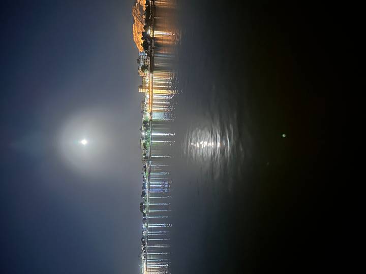 Nighttime river view with bright moon halo and city lights reflecting on calm water
