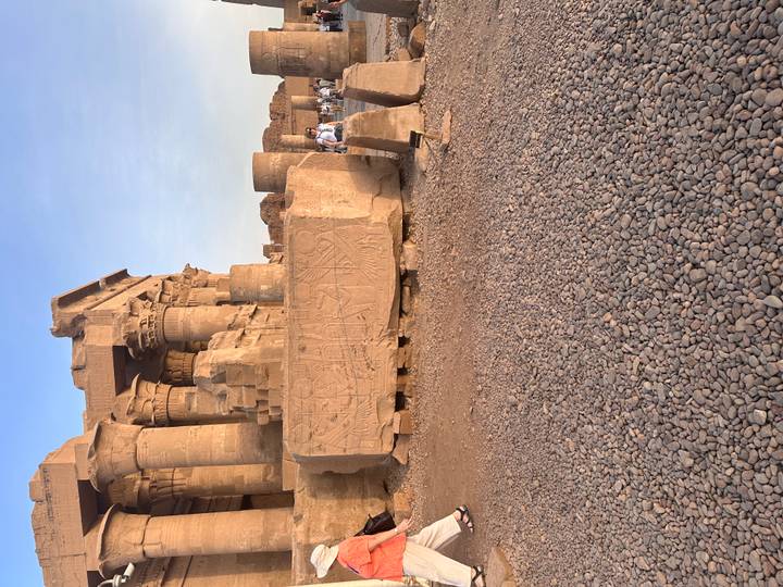 Expansive courtyard of Kom Ombo with carved stone blocks and visitors exploring