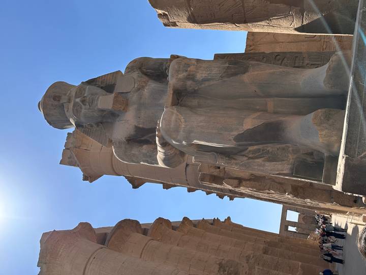 Towering seated pharaoh statue framed against deep blue sky at Luxor Temple