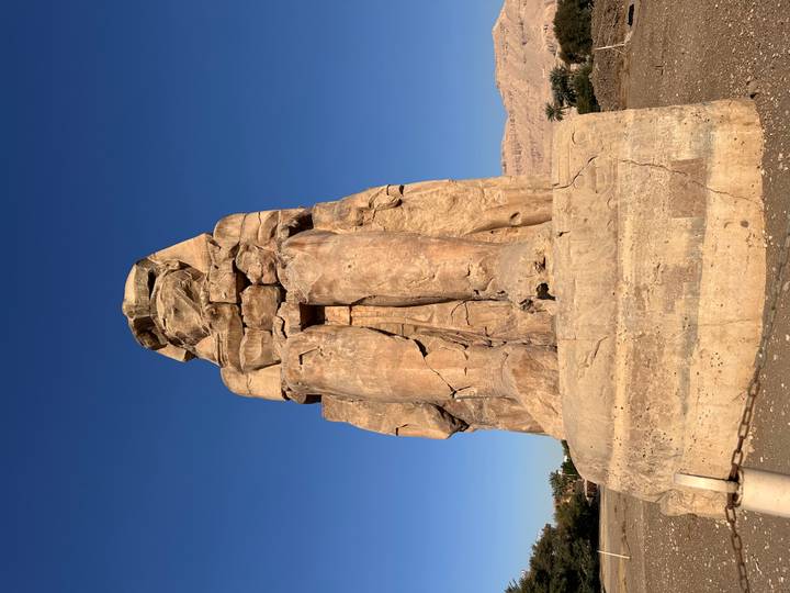 Massive Colossus of Memnon statue standing tall against clear desert sky