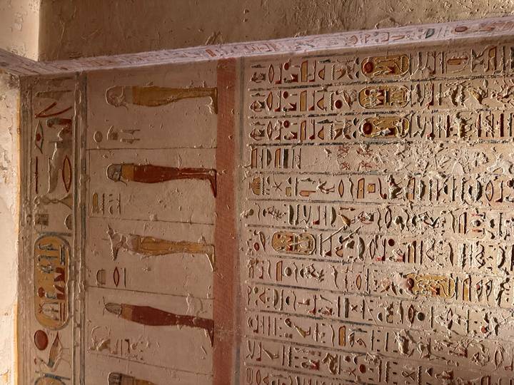 Wall covered in rows of colorful hieroglyphs and painted standing figures