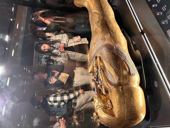 Visitors photographing an ornate golden sarcophagus displayed behind glass