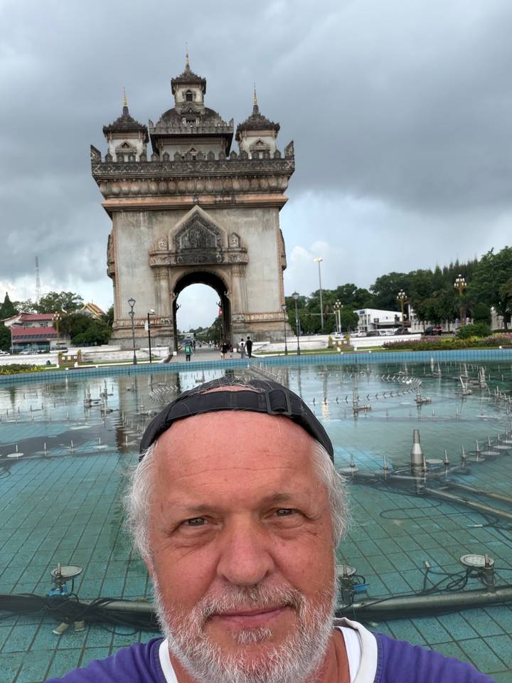 Partial selfie with head in foreground and Patuxai arch and fountain behind in Vientiane.