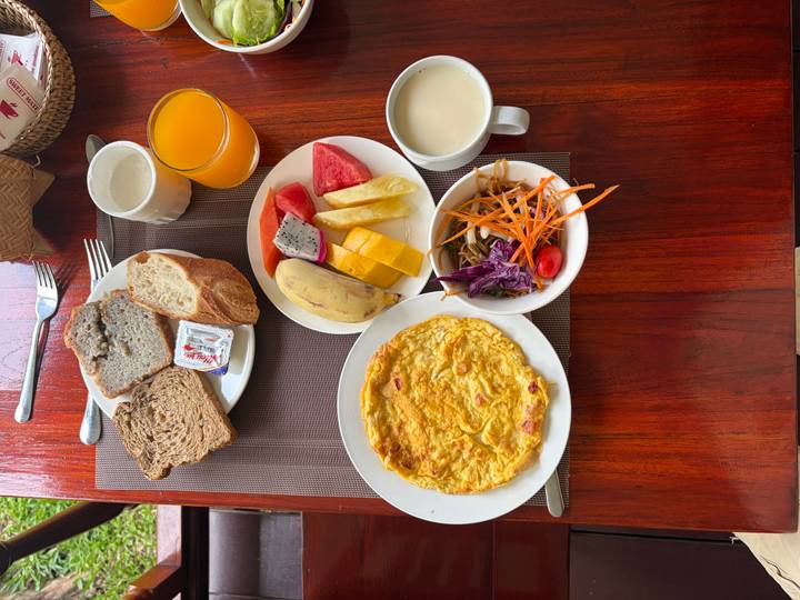 Top-down breakfast spread with omelette, fresh fruit, bread, juice and milk on wooden table.