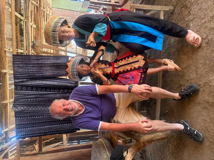 Similar portrait with tourist and hill-tribe girl posing peace sign next to textiles backdrop.