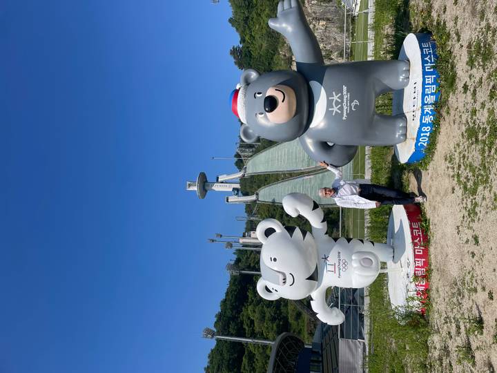 Visitor posing with Pyeongchang Olympic tiger and bear mascots before a ski jump tower