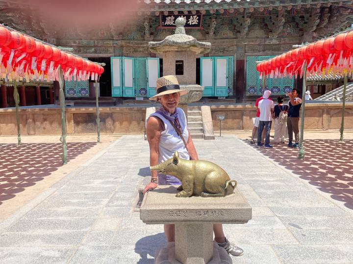 Tourists in a temple courtyard lined with red lanterns admiring a golden zodiac statue