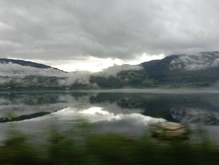 Moody grey clouds hover over still lake perfectly reflecting surrounding misty hills.