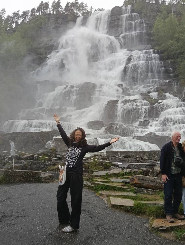 Tourist poses joyfully in front of roaring tiered waterfall with mist spraying everywhere.