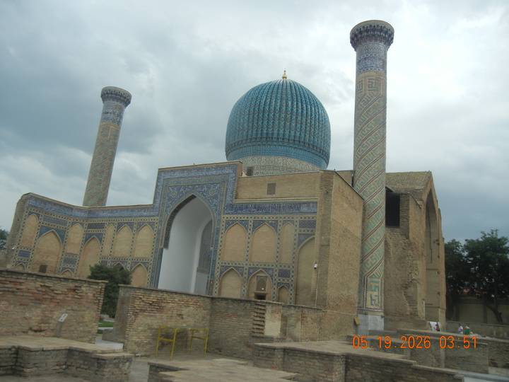Iconic Gur-e-Amir Mausoleum in Samarkand with blue tile dome and towering minarets beneath stormy sky.