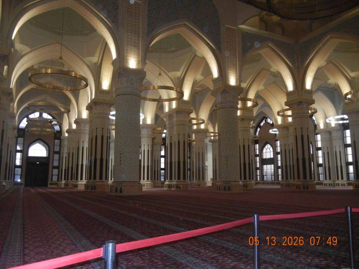 Lavish interior of grand mosque with tall columns, chandeliers and patterned carpet.