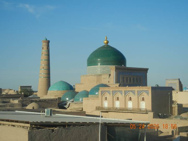 Skyline of Khiva with green-tiled domes and slender minaret glowing in morning light.