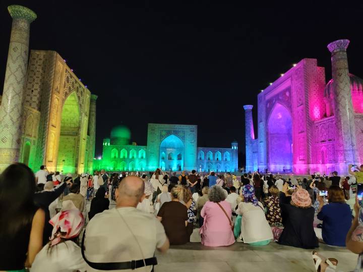 Nighttime light show bathes Samarkand's Registan in vibrant colours as crowd watches.