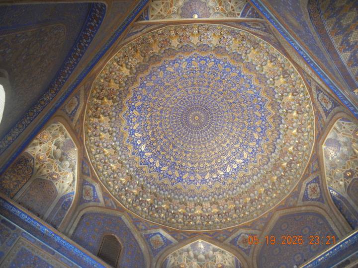Intricately decorated blue-and-gold Islamic dome ceiling with symmetrical geometric patterns.