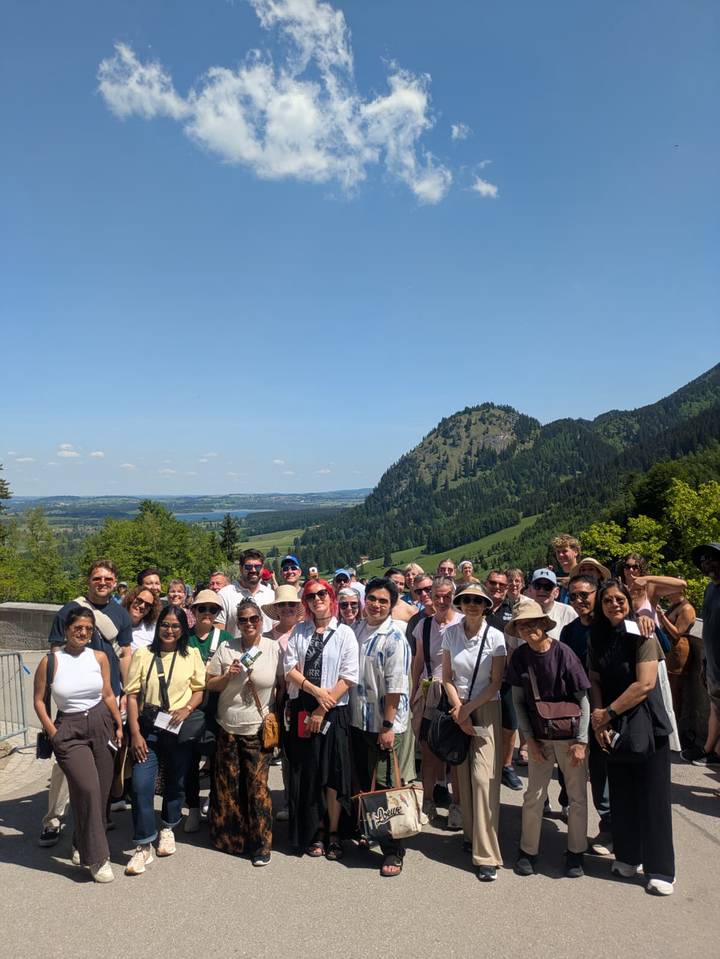 Large tour group posing on a viewing platform with rolling Bavarian hills, lakes and forests behind.