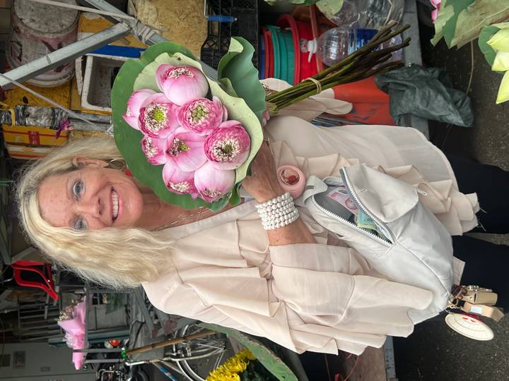 Smiling woman holding a bouquet of pink lotus flowers at a bustling street market.