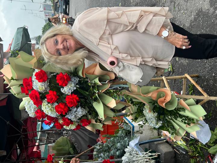 Woman posing beside a lavish arrangement of red, white, and blue flowers at an outdoor market.