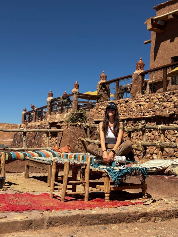 Woman seated on rustic desert terrace framed by stone walls and clear blue sky.