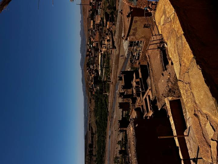 High vantage of earthen kasbah ruins overlooking a dry riverbed and distant village.