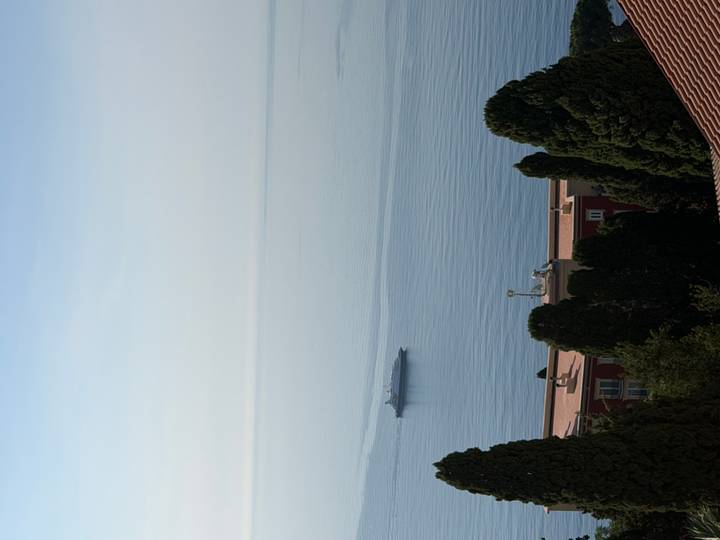 A lone cruise ship traverses calm, pale-blue open water under a clear morning sky.