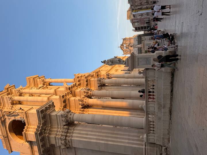 Baroque cathedral in Syracuse bathed in warm golden-hour light with visitors strolling the stone piazza.