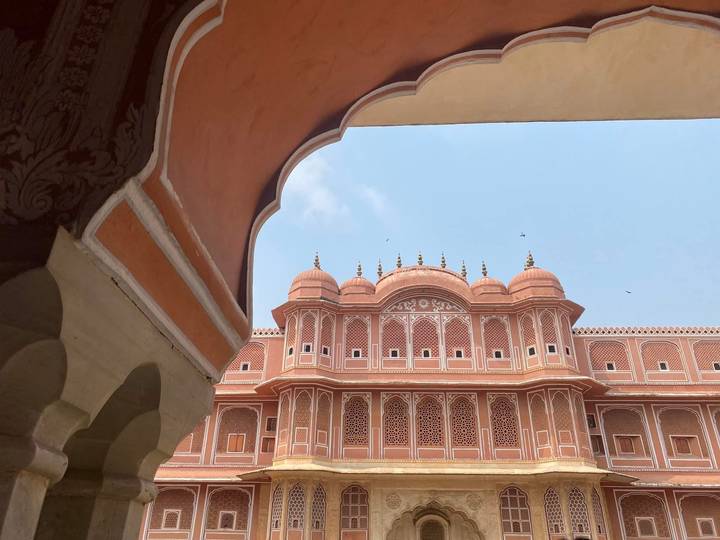 An ornate pink façade of a palace in Jaipur framed artistically by a scalloped arch against a blue sky.